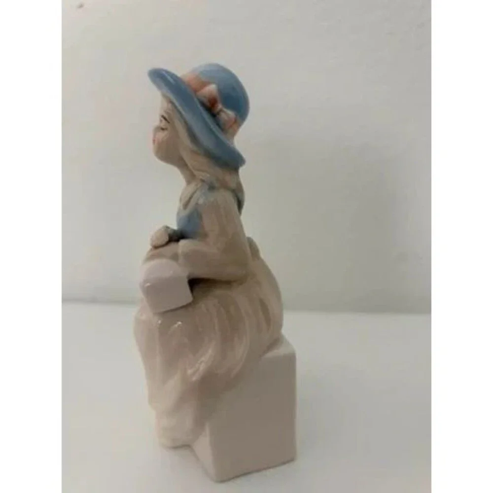 vtg. porcelain figurine of a seated girl wearing a blue hat